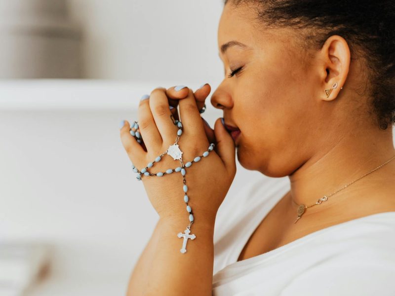 Close-up of a woman with eyes closed, holding rosary beads in prayer.