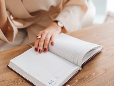 Adult woman writing in an open notebook at a wooden desk, focusing on reading and note-taking.