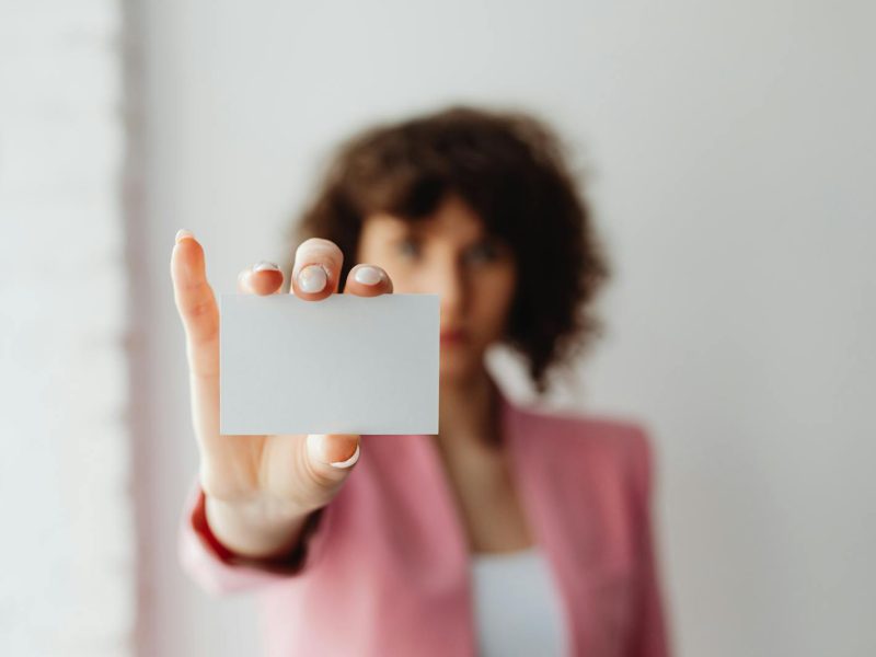 A professional woman in pink suit presenting a blank business card indoors.